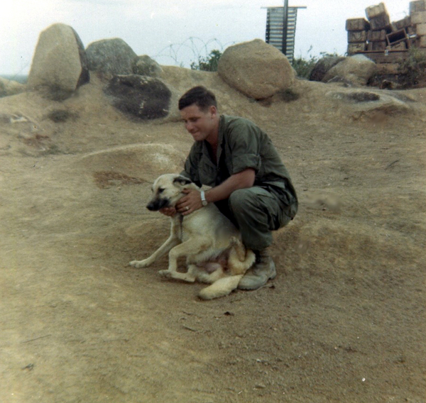 Popular Dog
Looks like we have yet another photo of "Short Round".  Much talk and I think a special place on the 2/9th web site for pics of unit adopted dogs. Here is another. This dog had several names as I recall... "Short Round" being one of them, but he had others as well. Guy with him here was a Commo member, but I cannot recall his name. Possibly Terry. If I remember, he was a lineman. He arrived shortly before went home. By this time, I believe the 'ol hard-ass sarge was gone or at least not somewhere close enough to have influence. He would have never allowed boots to look like that! Note the the "urinator" and ammo boxes in the background. I think this was at Kontum...
