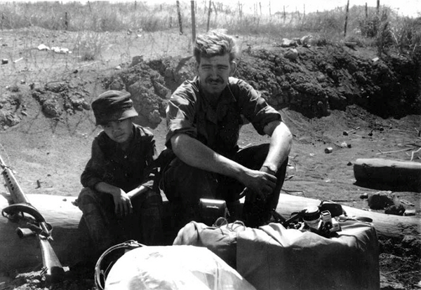 Man and boy
Paul Howe sits and chats with a young boy scout.  Behind them is the ubiquitous concertina wire to identify a perimeter.
